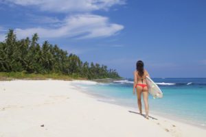 Girl walking on white beach with surfboard