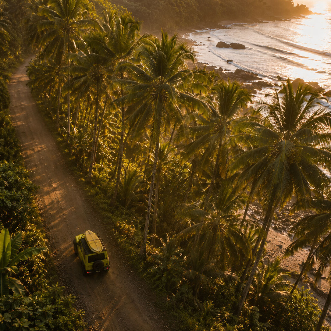 Drone view of a 4x4 driving along a tropical jungle road beside the ocean in Costa Rica during golden hour