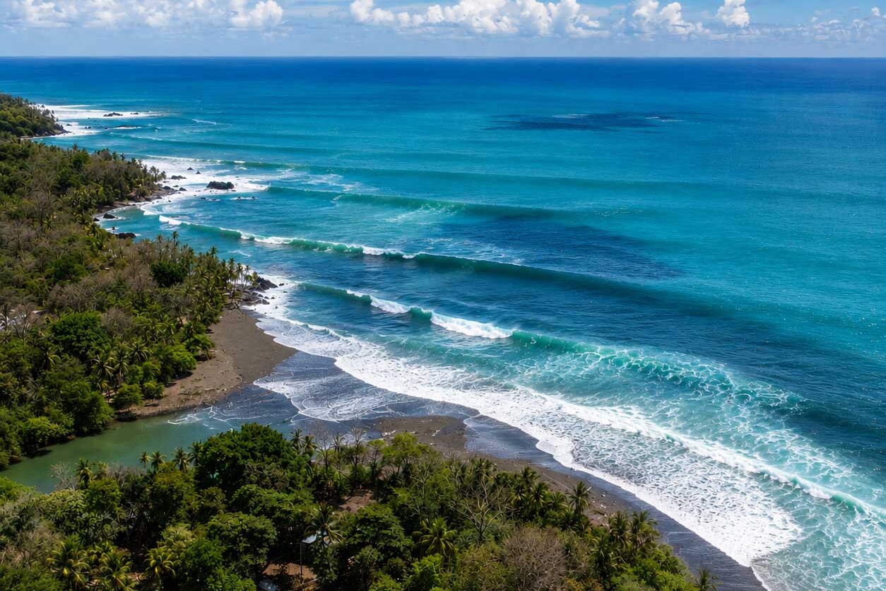 Aerial view of Pavones, Costa Rica with tropical jungle, black sand beach and long left-hand surf waves.